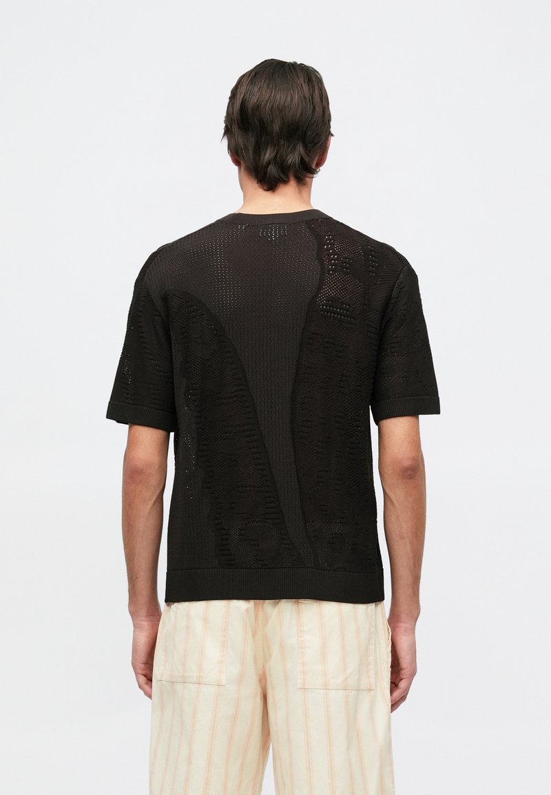 Pull en tricot noir à manches courtes avec un motif perforé et un ourlet côtelé. Il présente des détails texturés et une coupe décontractée.