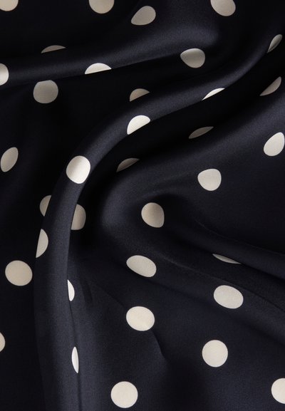 Tissu noir soyeux avec des pois blancs, présentant des plis doux et une texture lisse.