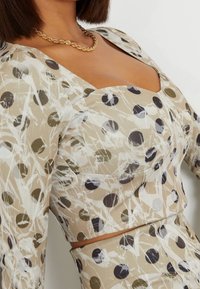 Top beige claro con escote cuadrado, que presenta un divertido patrón de lunares en negro, verde y blanco. Tela suave con un diseño ajustado.