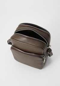 Brun skinn crossoverveske med to glidelåslommer, jevn tekstur og glidelåser i sølvfarge. Kompakt design for praktisk bruk.