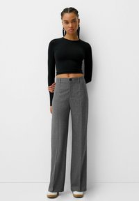 Crop top noir à manches longues associé à un pantalon large gris à rayures avec une fermeture à bouton à l'avant et un tissu texturé.