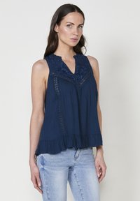 Top senza maniche di colore blu navy con scollatura ricamata, dettagli in pizzo, orlo svasato e tessuto strutturato.