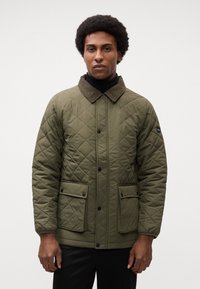 Olivenfarvet quiltet jakke med en kordfløjlskrave, frontknapper og to store klaplommer. Glat tekstur, mellemlang design.