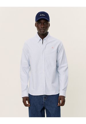 Chemise à rayures bleu clair avec un petit logo rouge. Portée avec une casquette marine ornée de texte brodé blanc et un jean en denim décontracté.