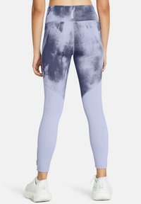 Leggings taille haute en violet clair avec un motif tie-dye sombre. Présente des détails perforés sur les côtés et un tissu lisse et extensible.