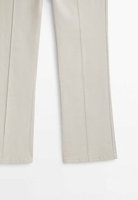Pantalon beige en mélange de coton, présentant une coupe droite, des coutures visibles et sans poches extérieures.
