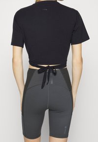 Svart kortärmad topp med knyt baktill, tillsammans med högmidjade grå cykelbyxor med paneldetaljer och sömmar.