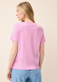 Camiseta de algodón rosa de manga corta con cuello redondo y un corte relajado. La tela tiene una textura suave con un ligero brillo.