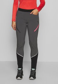 Šedé sportovní legíny s černo-bílým akcentem a růžovou kapsou se zipem, doplněné černými sportovními botami.