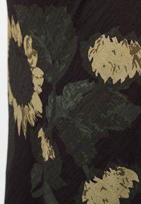 Σκούρο ύφασμα με υφή που παρουσιάζει μεγάλα μπεζ ηλιοτρόπια και πράσινα φύλλα.