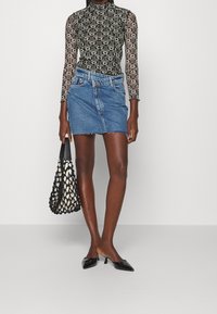Femme portant un haut à manches longues noir et blanc à motifs, une mini-jupe en denim asymétrique, des talons aiguilles noirs et portant un sac à main en filets noir.