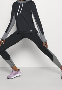 Svart och grå hoodie med en framficka och vita dragsko, tillsammans med svarta och grå leggings. Rosa träningsskor med svarta accenter.