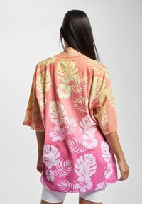 Oversized, short-sleeve t-shirt with a gradient from orange to pink, featuring white tropical leaves and hibiscus flowers in a textured print.