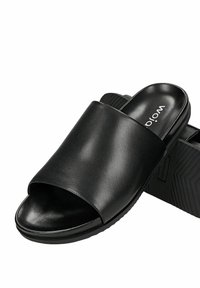 Sandales slides noires à bout ouvert avec une large bride en cuir et des semelles texturées, affichant le nom de la marque "Wojo" sur la semelle intérieure.