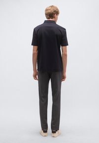 Sötétkék, rövid ujjú, egyenes szabású galléros póló, amelyet szürke nadrággal és bézs cipővel párosítanak, finom textúrával.