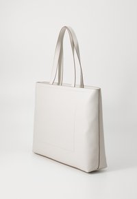 Borsa a tote in pelle sintetica crema con manici doppi, forma quadrata, cuciture visibili e accenti testurizzati sottili.