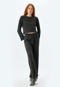 Kaksi-osainen loungwear-setti tummanharmaasta ribbikangasesta. Topissa on pitkät hihat ja röyhelöhelma; housuissa on joustava vyötärö ja leveät lahkeet.