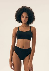 Schwarzer BH mit dünnen Trägern und passenden hochgeschnittenen Slip, aus glattem Material mit minimalen Nähten und einem eleganten Design.