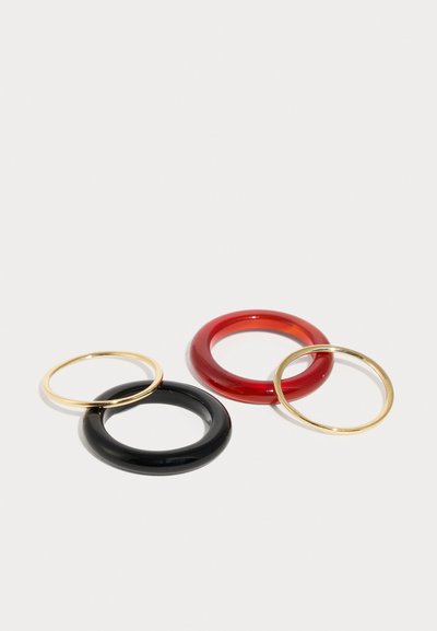 Τρία δαχτυλίδια: ένα μαύρο και ένα κόκκινο από γυαλιστερό υλικό, καθώς και δύο δαχτυλίδια από χρυσό μέταλλο. Τα σχήματα είναι κυκλικά με ομαλές άκρες.