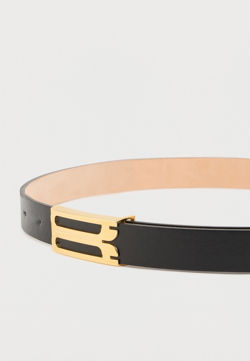 Ceinture en cuir noir avec une boucle en métal doré présentant un design ajouré. Le côté intérieur est lisse et de couleur claire pour le contraste.
