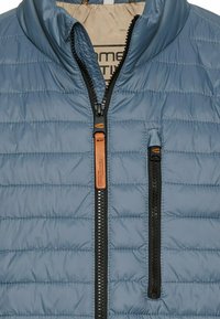 Blauwe geïsoleerde vest met een horizontaal quiltpatroon, hoge kraag en twee ritszakken. Inclusief zwarte rits met leren accent.