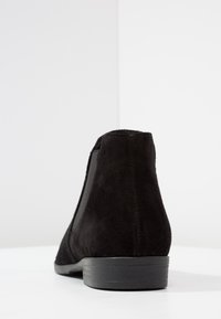 Stivaletto in suede nero con pannelli laterali elastici e un tacco basso e testurizzato. Presenta una silhouette liscia e una finitura opaca.