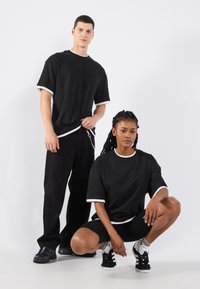 Tricouri negre din bumbac cu detalii albe, având o croială lejeră. Modelul masculin poartă pantaloni negri, iar modelul feminin poartă pantaloni scurți negri cu șosete.