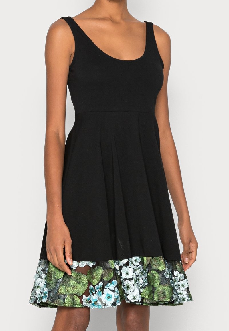 Robe noire sans manches avec un décolleté rond et un ourlet orné de dentelle florale verte et blanche.