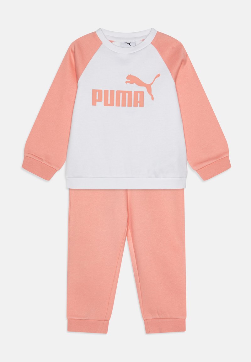 Gaismas kokvilnas trenerku komplekts, kurā ietilpst balts krekls ar korallkrāsas raglan piedurknēm un lielu "PUMA" logotipu, saskaņots ar korallkrāsas biksēm.