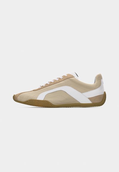 Μπεζ και λευκό χαμηλό sneaker με καφέ λαστιχένια σόλα, κλείσιμο με κορδόνια και κυματιστό σχέδιο στο πλάι πάνω σε μονόχρωμο φόντο.