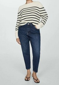 Crème trui met zwarte strepen, gecombineerd met donkerblauwe jeans met hoge taille. De outfit heeft een relaxte pasvorm en eenvoudige teenslippers.