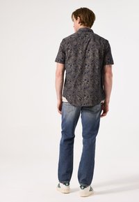 Korte mouwen button-up overhemd in donker marineblauw met een bladdessin; relaxte pasvorm; gedragen met lichtblauwe jeans en sneakers met groene accenten.