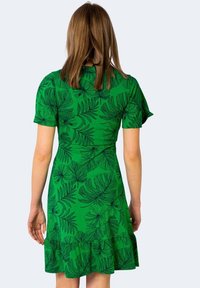 Zelené šaty s potiskem listů, krátkými rukávy, těsným živůtkem a rozšířenou sukní se volánem na lemu.