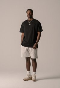 Black cotton t-shirt, loose fit, with a small logo. Light gray shorts, soft texture. Tan sneakers with light accents and white socks.
