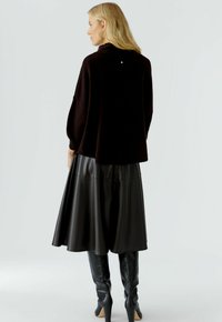 Übergroßer schwarzer Pullover mit hohem Kragen und Rückendetaillierung, kombiniert mit einem schwarzen Leder-Midirock und kniehohen schwarzen Stiefeln.