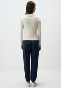 Top a maniche lunghe bianco a coste abbinato a pantaloni blu con polsini elasticizzati e sneakers bianche. Design semplice con colori neutri e vestibilità comoda.