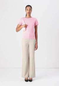 T-shirt en coton rose à manches courtes, associé à un pantalon large beige et des chaussures à talons noires, portant un petit sac à main blanc.