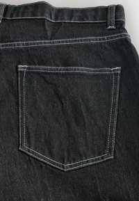 Czarne dżinsy o właściwościach denim z jedną tylną kieszenią z kontrastowym białym przeszyciem. Materiał wydaje się lekko fakturowany i trwały.