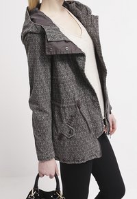 Gray patterned jacket with a hood, featuring a zip closure, side pockets, and brown accents. Complemented by a black handbag.
