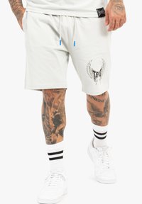 Heledad hallhalli hallhalli mõttes TAPOUT logo ja tiibade kujundusega, elastse vöökohtadega ja paeltega. Kandmine valgete tossudega ja triibuliste sokkidega.