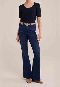 Tummansinisiä levennettyjä farkkuja, jotka on yhdistetty mustaan lyhythihaiseen teksturoituun puseroon ja vaaleanbeigeen vyöhön, jossa on pyöreä kullanvärinen solki.