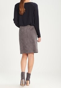 Marinebluse mit langen Ärmeln, kombiniert mit einem grauen Wildleder-Pencilrock. Graue Stiefeletten mit metallischen Roségold-Absätzen runden den Look ab.