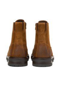 Paire de bottines en daim marron vues de dos, avec des semelles en caoutchouc brun foncé et des détails cousus.