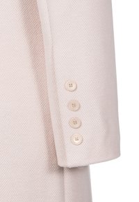 Ljusrosa textiler med en fiskbensmönster. Fyra runda knappar i en ljus nyans på manschetten, som visar en skräddarsydd design.