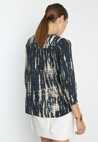 Tmavě modrá a krémová tie-dye blůza s třičtvrtinovými rukávy, volným střihem a jemným skladem vzadu. Hladká textura.