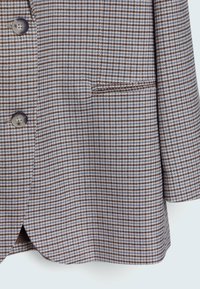 Blazer à motif pied-de-poule marron et bleu avec trois boutons gris foncé et une poche passepoilée à l'avant côté droit.