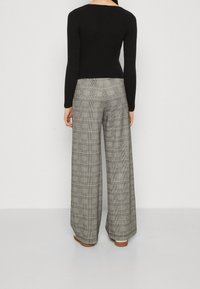 Svart ribbad tröja med lång ärm, tillsammans med rutig vida byxor i grått och vitt, med en strukturerad passform och mjuk textur.