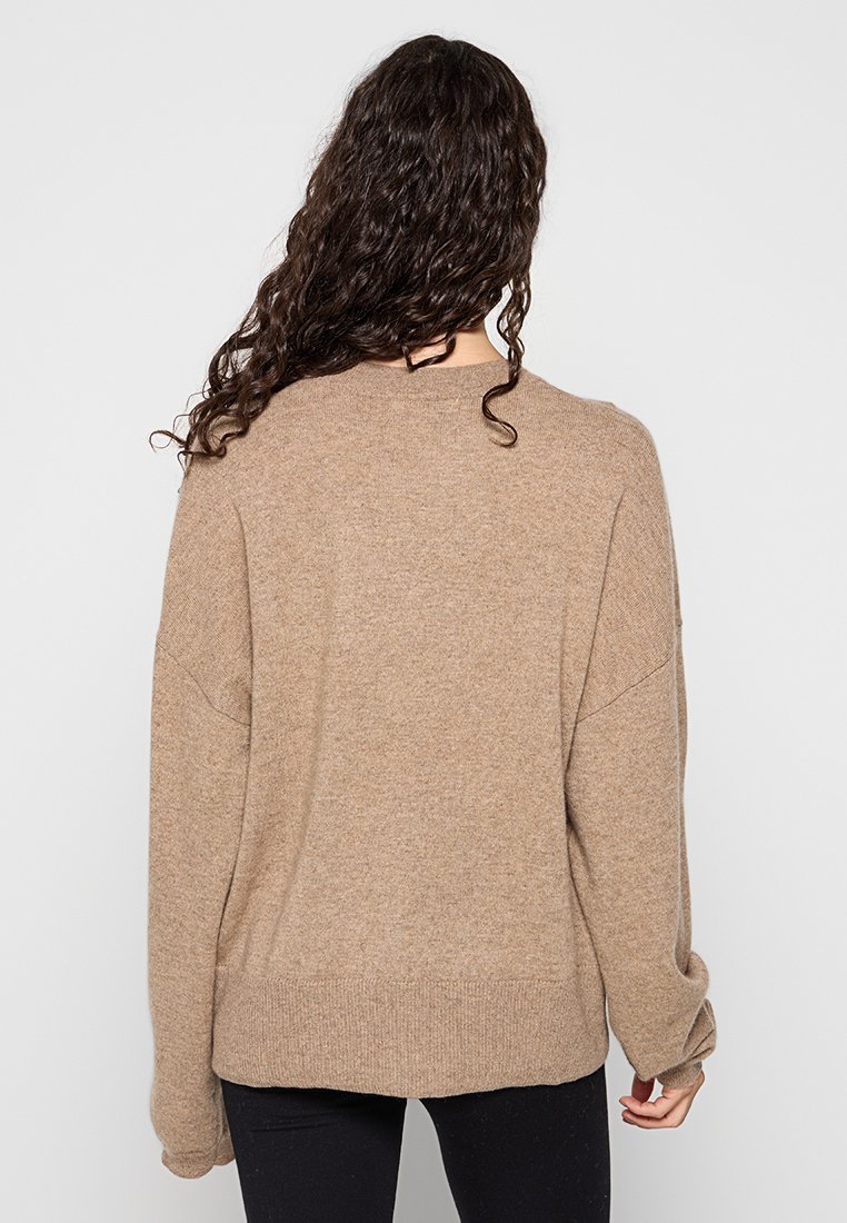 Maglione oversize marrone chiaro con scollo rotondo, polsini e orlo a coste, caratterizzato da una morbida texture in maglia e spalle abbassate.