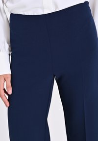 Pantalons ajustés bleu marine en tissu léger, avec une texture lisse et une légère éventuelle au bas, dotés d'une taille propre.