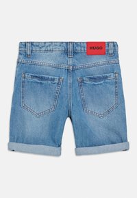 Shorts in denim blu chiaro con orlo arrotolato, dotati di due tasche posteriori, cuciture arancioni e un'etichetta rossa con "HUGO" sulla vita.